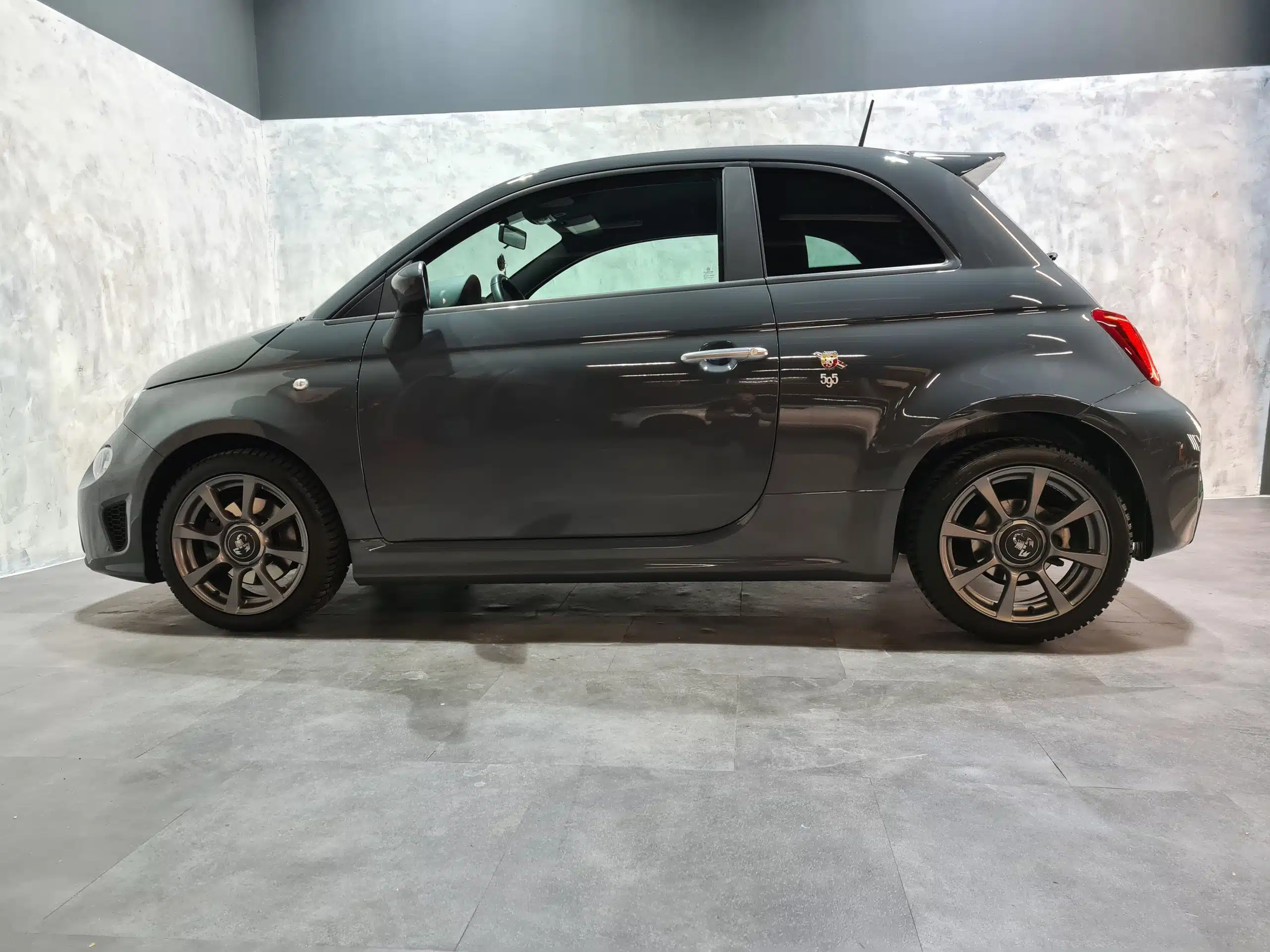 Grauer Fiat 500 Abarth 595 in einer Fotobox mit grauem Betonboden und hellem Struktur-Hintergrund, seitlich fotografiert.