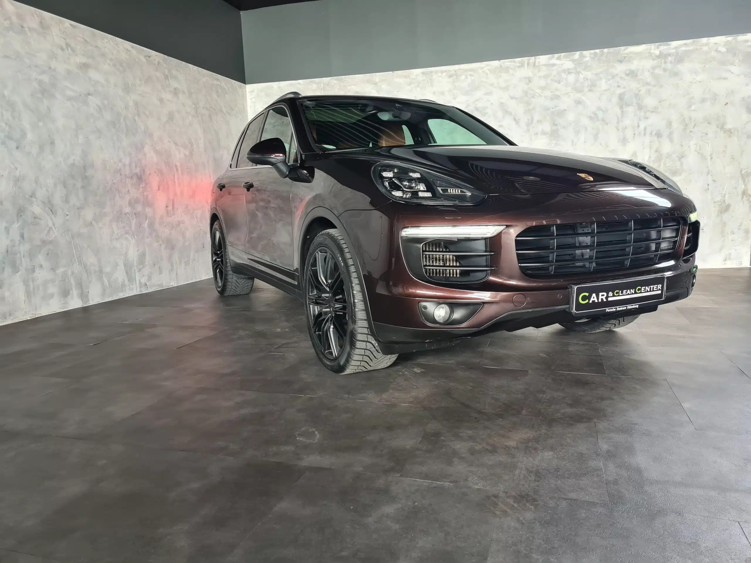 Dunkelroter Porsche SUV nach professioneller Fahrzeugaufbereitung im Showroom des Car & Clean Centers.