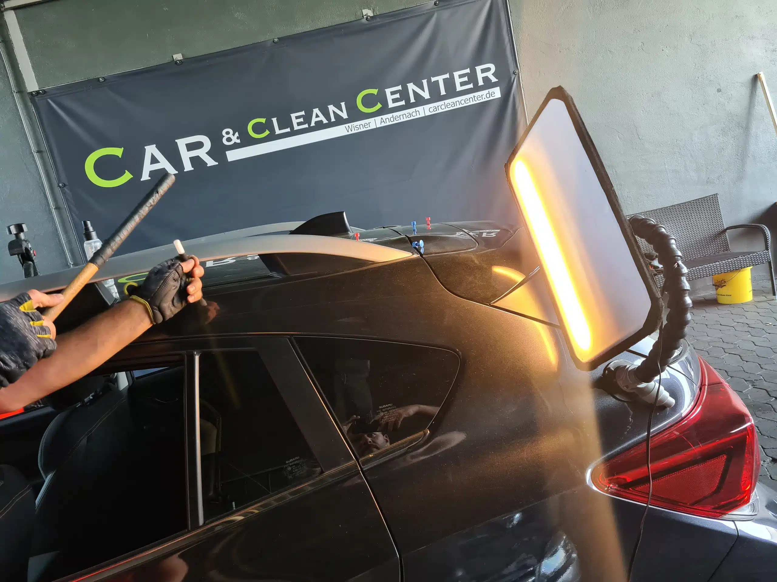 Nahaufnahme einer PDR-Reparatur am Fahrzeugdach, Mechaniker arbeitet mit Werkzeug und LED-Kontrollleuchte.