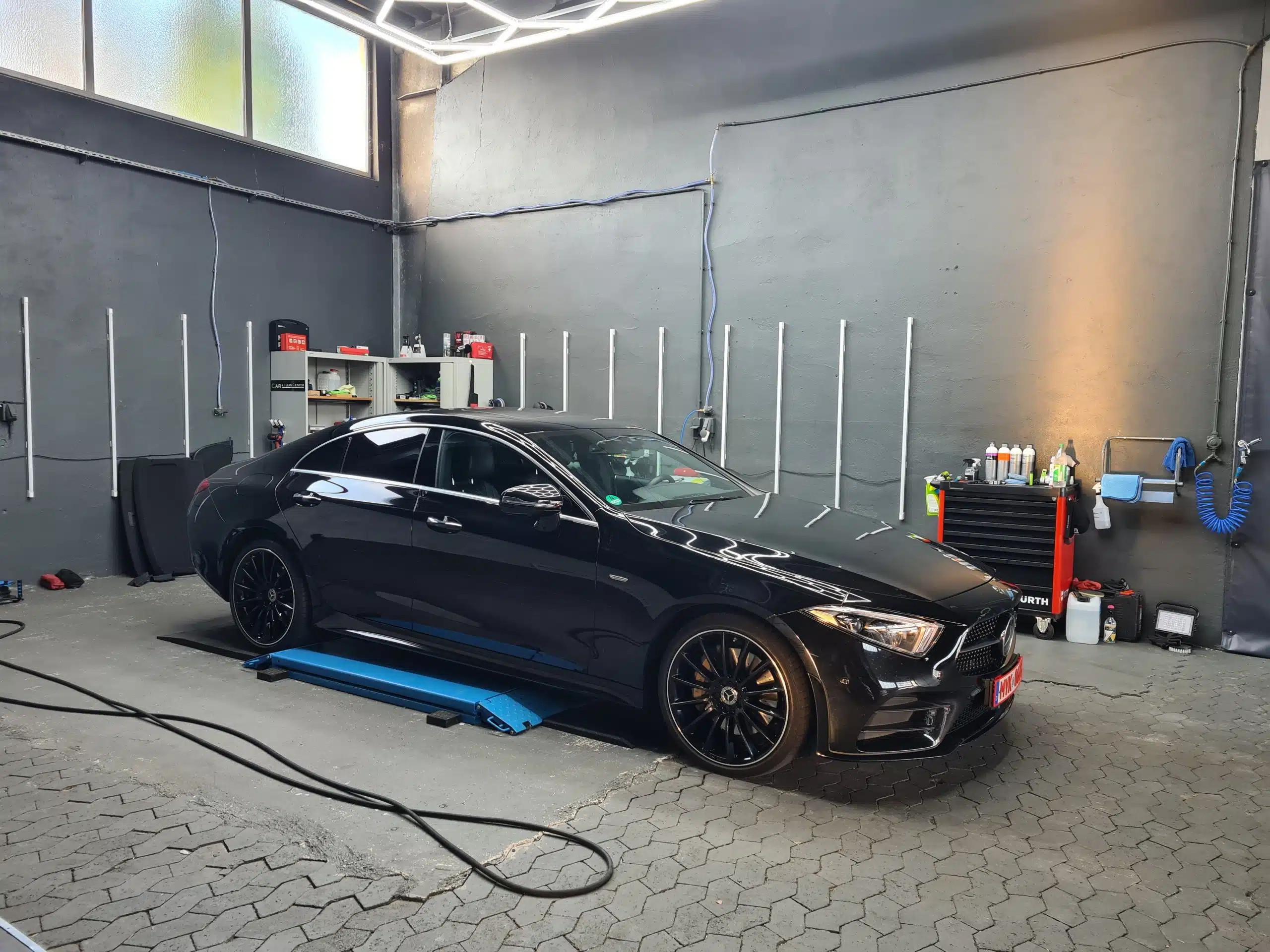 Schwarzer Mercedes in einer professionell ausgestatteten Detailing-Werkstatt auf einer Niedrighebebühne.