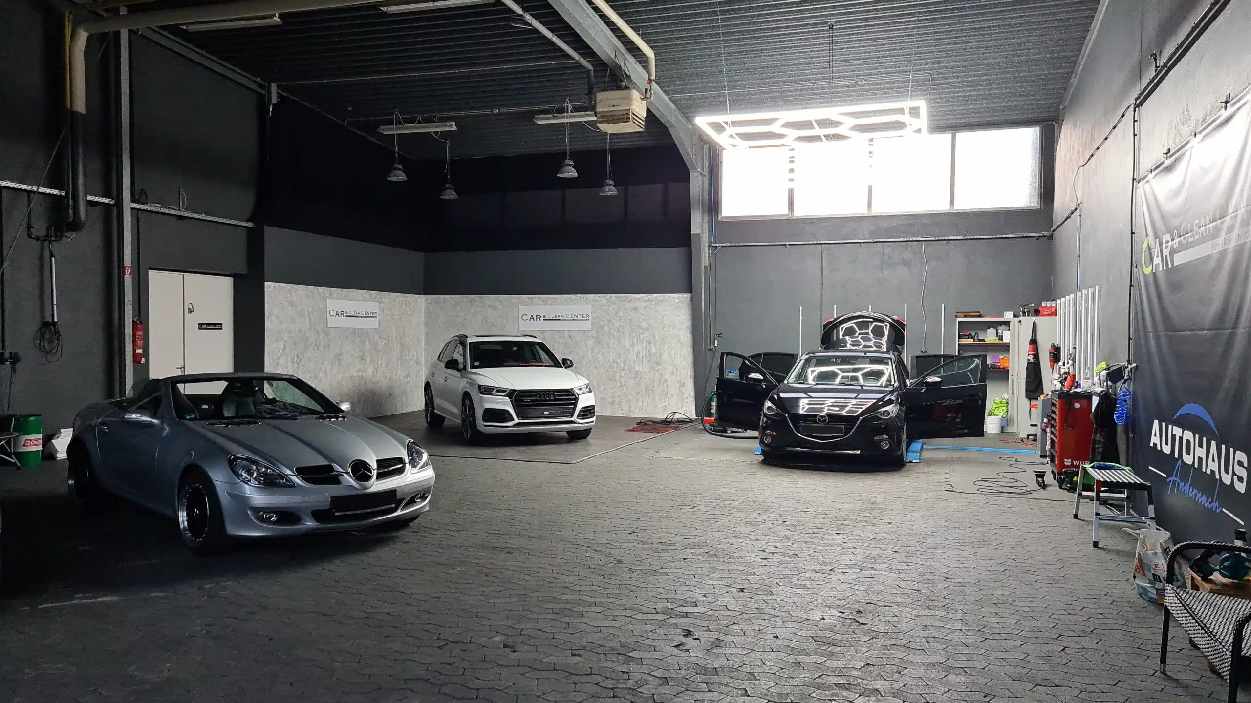 Fahrzeugaufbereitungshalle mit mehreren Fahrzeugen bei Car & Clean Center – Mercedes, Audi und Mazda in der professionellen Bearbeitung.