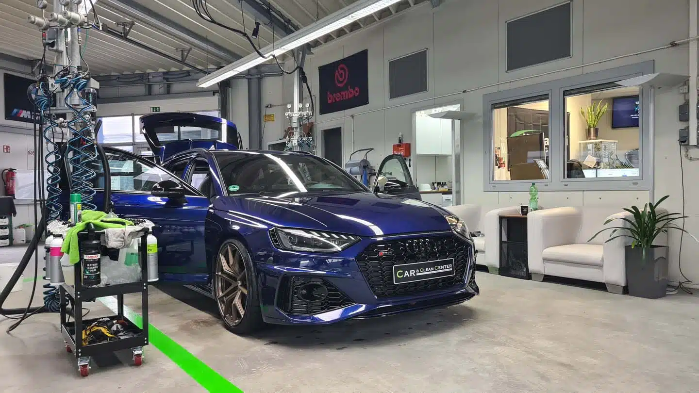 Blauer Audi Sportwagen in der Aufbereitungshalle des Car & Clean Centers, umgeben von professionellem Detailing-Equipment.
