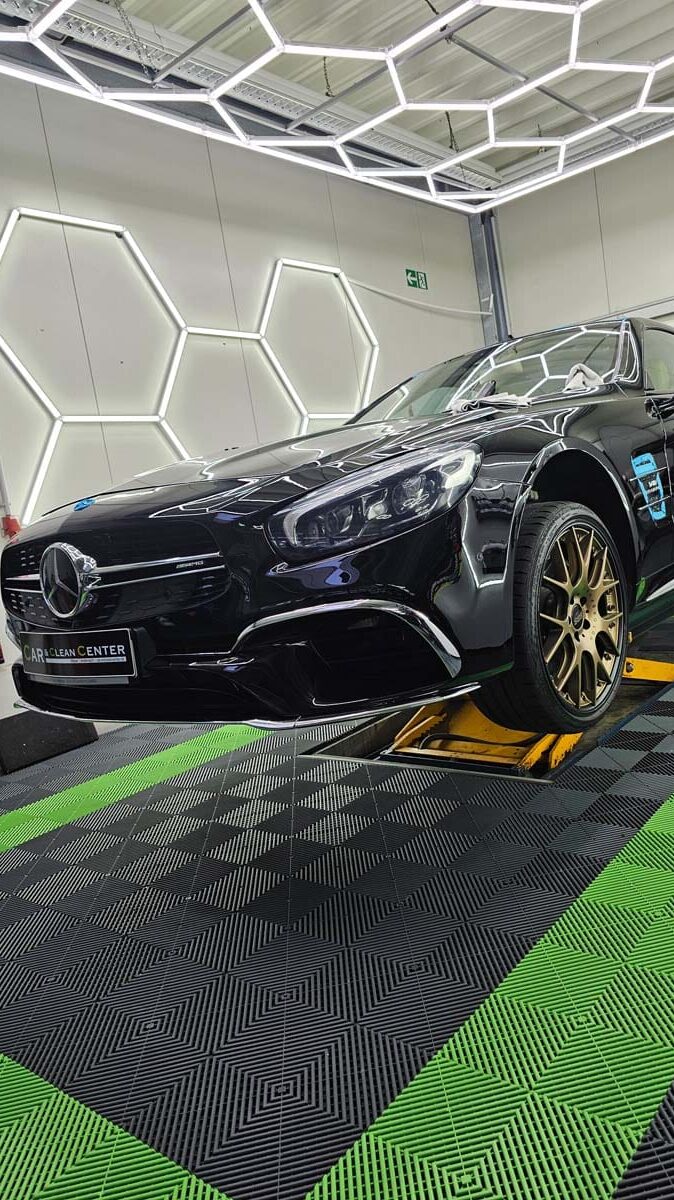 Schwarzer Mercedes-AMG auf Hebebühne im modernen Detailing-Studio mit hexagonaler LED-Beleuchtung.