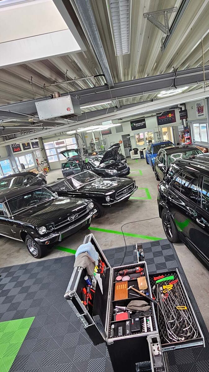 Mehrere schwarze Fahrzeuge, darunter Klassiker und Sportwagen, im Detailing-Bereich des Car & Clean Centers, umgeben von professionellem Equipment.
