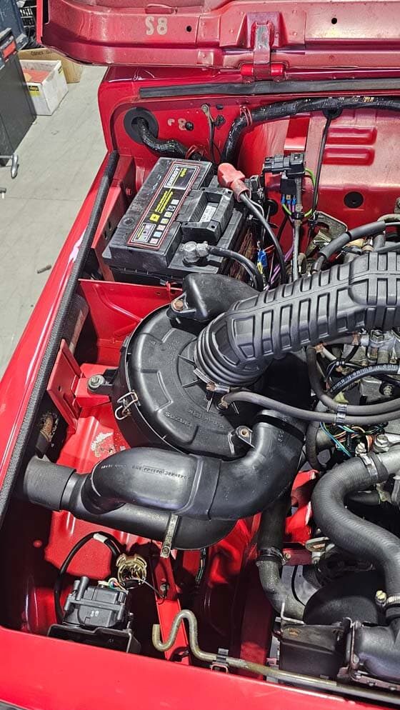 Motorraum eines roten Fahrzeugs nach Reinigung, mit sichtbarer Batterie, Luftfiltereinheit und sauberen Bauteilen.