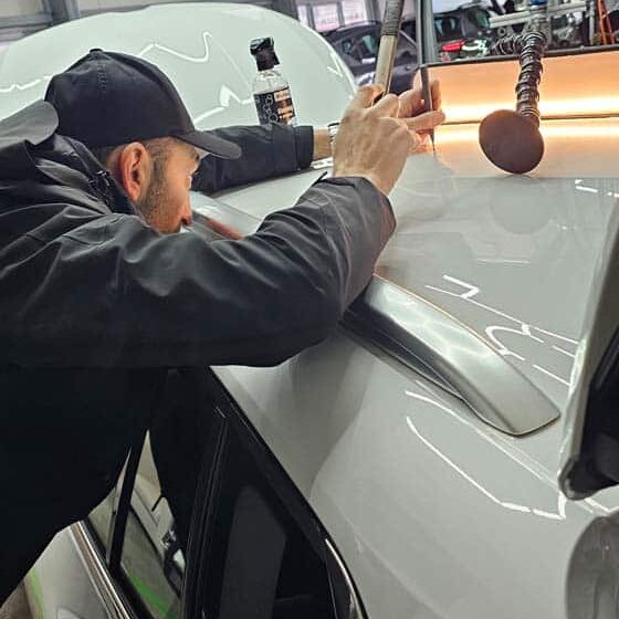 Techniker führt präzise Dellenentfernung am Fahrzeugdach mit Spezialwerkzeug und Ausbeullampe durch.