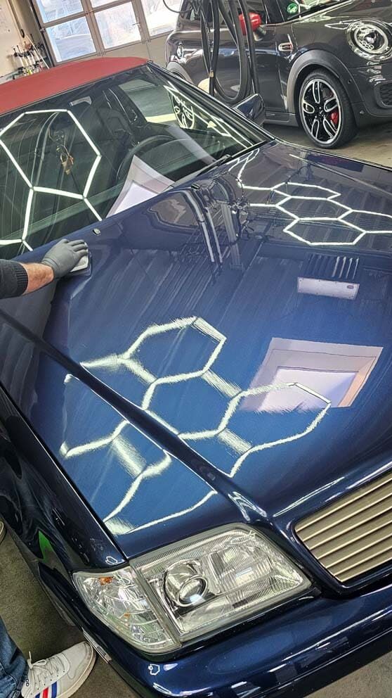 Aufbereitung eines blauen Mercedes mit hochglänzendem Lackfinish unter hexagonaler LED-Beleuchtung.