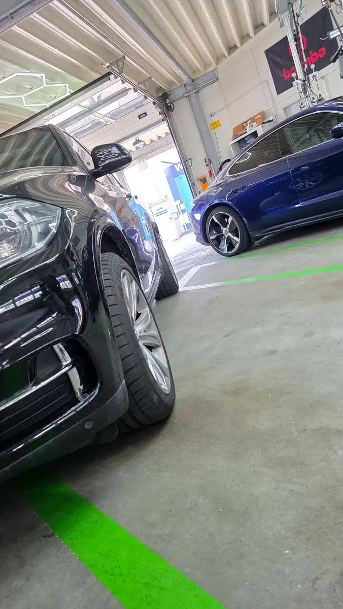 Zwei hochwertige Fahrzeuge in der Aufbereitungshalle, ein schwarzer SUV und ein blauer Sportwagen, bereit für professionelle Fahrzeugpflege.