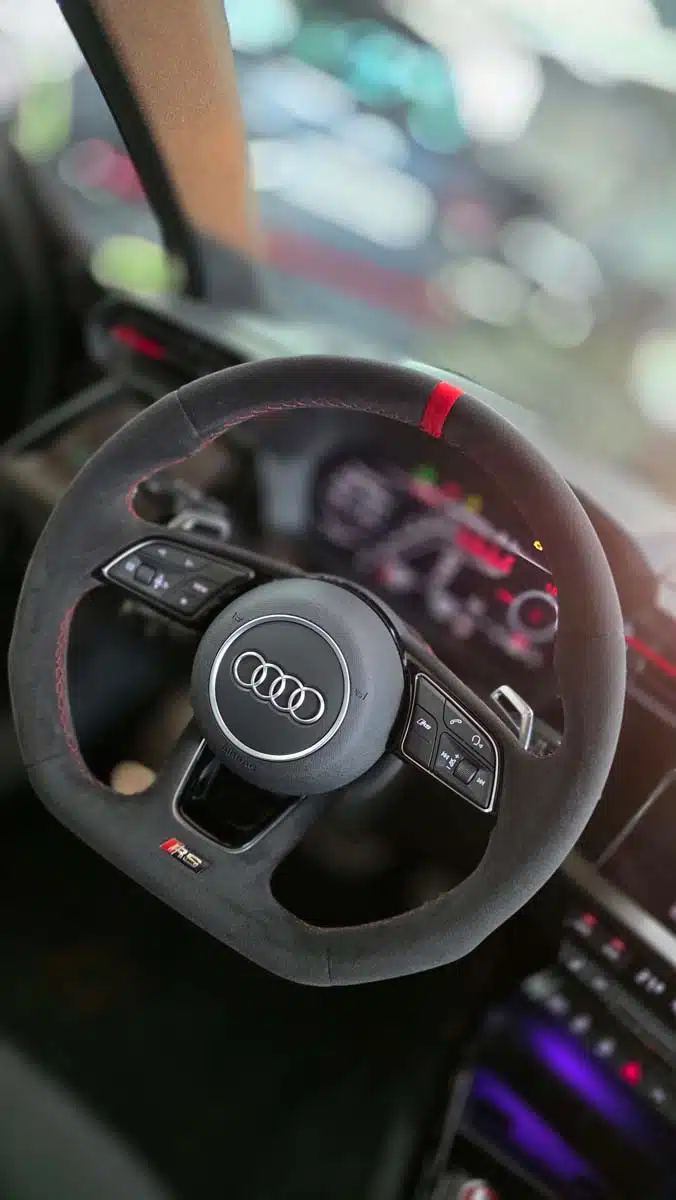 Detailaufnahme eines gereinigten Audi RS-Lenkrads im Innenraum, mit Alcantara und roter Markierung.